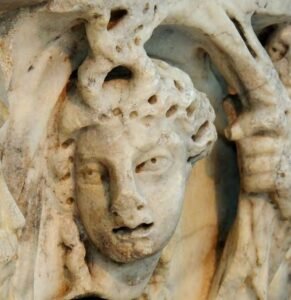 Primer plano en detalle de la cabeza esculpida en mármol de una nereida romana, perteneciente al sarcófago de Medina Sidonia, donde se aprecian los orificios y surcos profundos realizados con la técnica del trépano en el cabello.