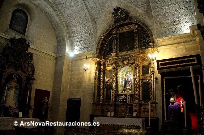 Interior de la capilla de la Hermandad de la Oración en el Huerto en Santo Domingo, Jerez, mostrando el retablo central iluminado y los pasos laterales con imágenes titulares, con la marca de agua de Ars Nova Restauraciones.