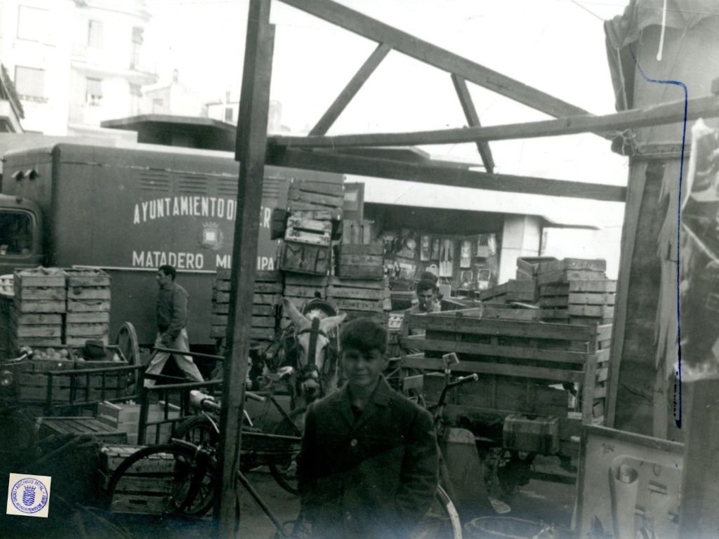 Fotografía histórica de la calle Doña Blanca en Jerez con furgonetas de reparto y multitud frente a la Plaza de Abastos en 1962.