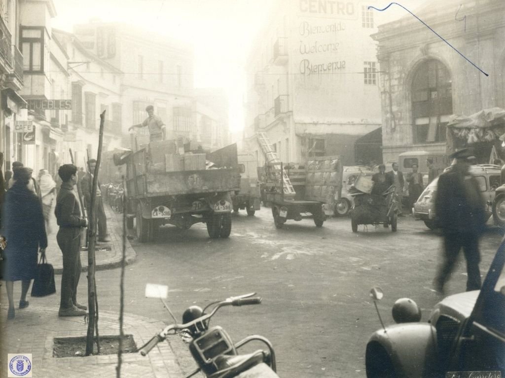 Camión de carga con matrícula CA-5516 circulando por la calle Doña Blanca en 1962, con operarios descargando mercancía frente al Mercado de Abastos y el cartel del Hotel Garage Centro al fondo.