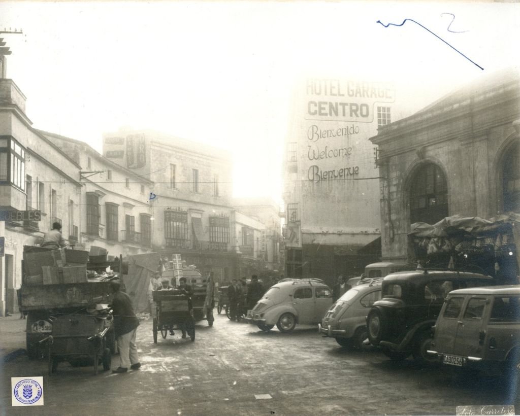 Fotografía en blanco y negro de la calle Doña Blanca en Jerez, 1962, capturando el Hotel Garage Centro con su cartel multilingüe ("Bienvenido", "Welcome", "Bienvenue") y coches de época aparcados como un Renault 4CV y furgonetas.