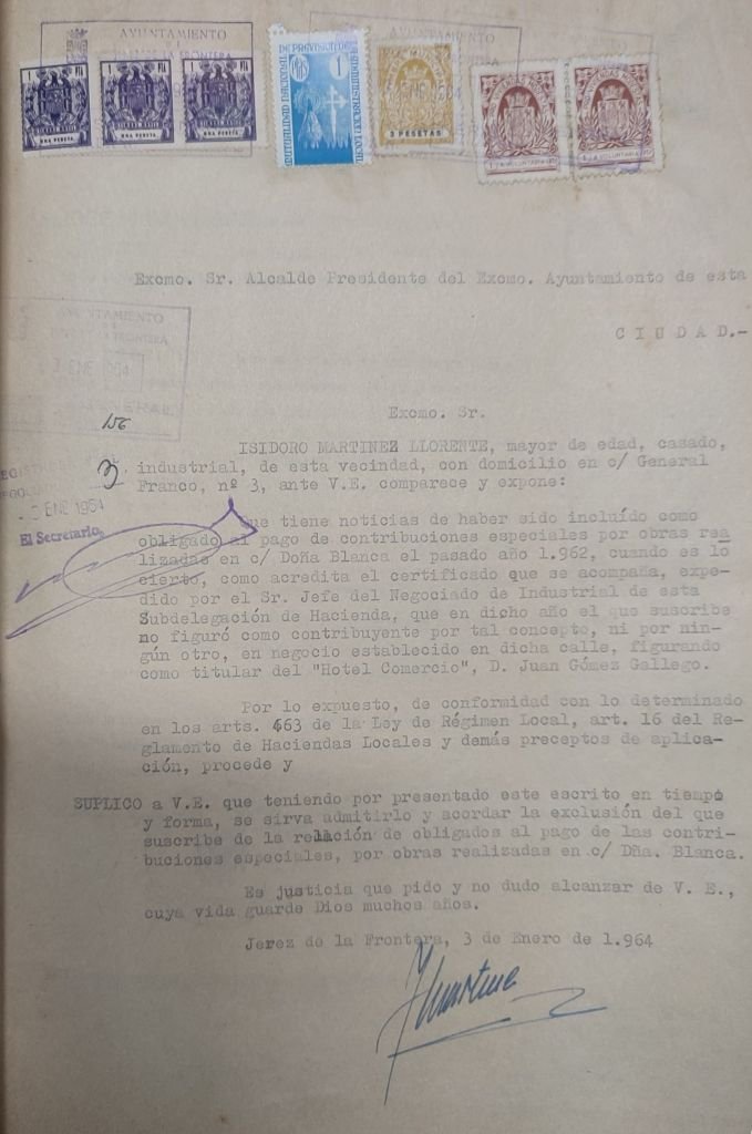 Escrito mecanografiado de enero de 1964 dirigido al Alcalde de Jerez, donde Isidoro Martínez Llorente solicita la exclusión del pago de contribuciones especiales por las obras de la calle Doña Blanca. El documento muestra varios sellos y pólizas de la época en la parte superior.
