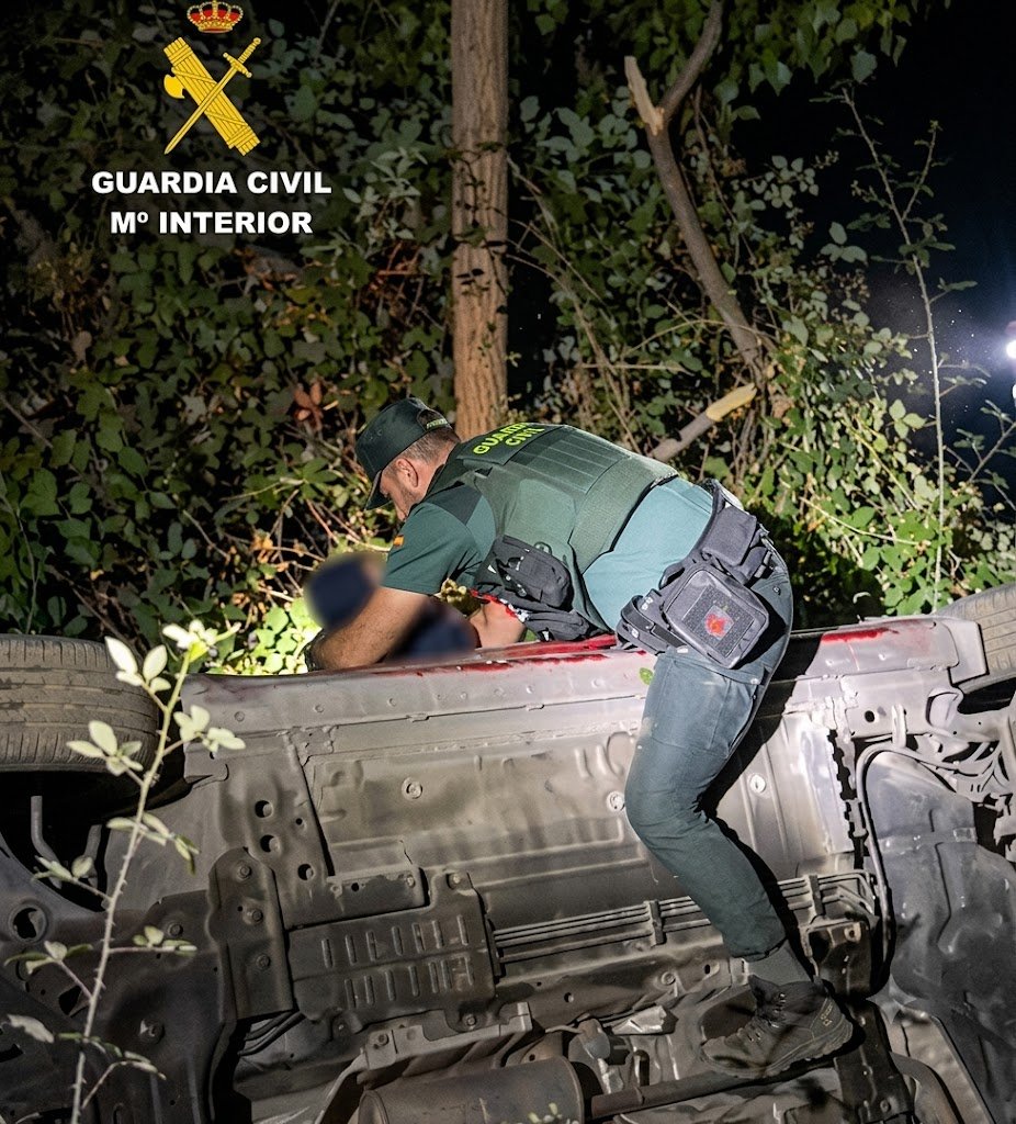 Agente de la Guardia Civil subido a un coche volcado durante un rescate nocturno en un terraplén de Granada.