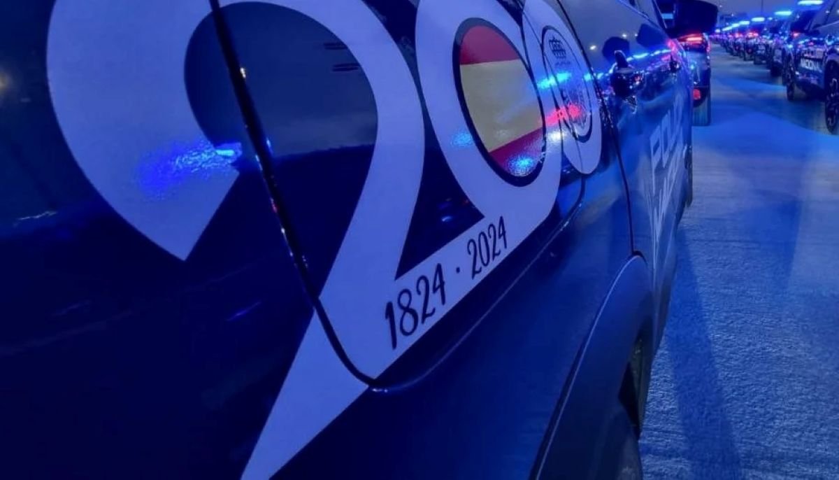Detalle de un coche patrulla de la Policía Nacional iluminado con luces azules, mostrando en su lateral el logotipo conmemorativo de su 200 aniversario (1824-2024).