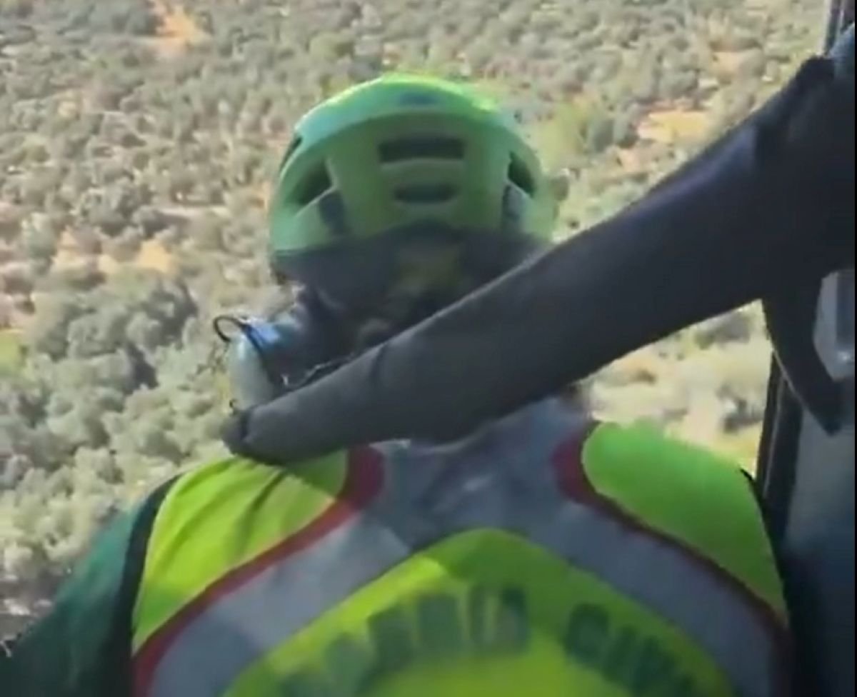 Miembro de la Guardia Civil con casco y chaleco reflectante a bordo de un helicóptero durante un rescate sobre un área montañosa.