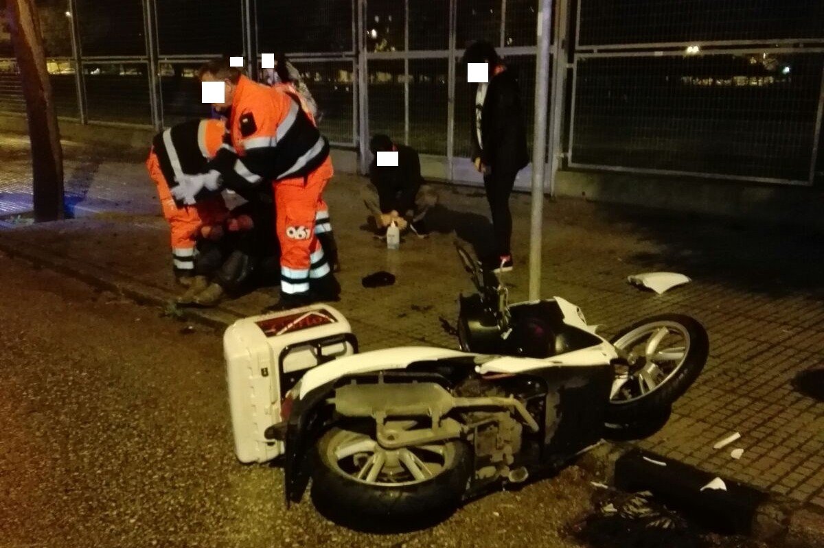 Servicios de emergencias sanitarias atendiendo a un motorista herido en el suelo tras un accidente de tráfico nocturno en Jerez, junto a su motocicleta de reparto volcada.