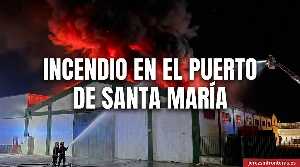 Fotografía nocturna de los bomberos extinguiendo un grave incendio en la cubierta de una nave industrial en El Puerto de Santa María, con llamas rojas e intensa humareda.