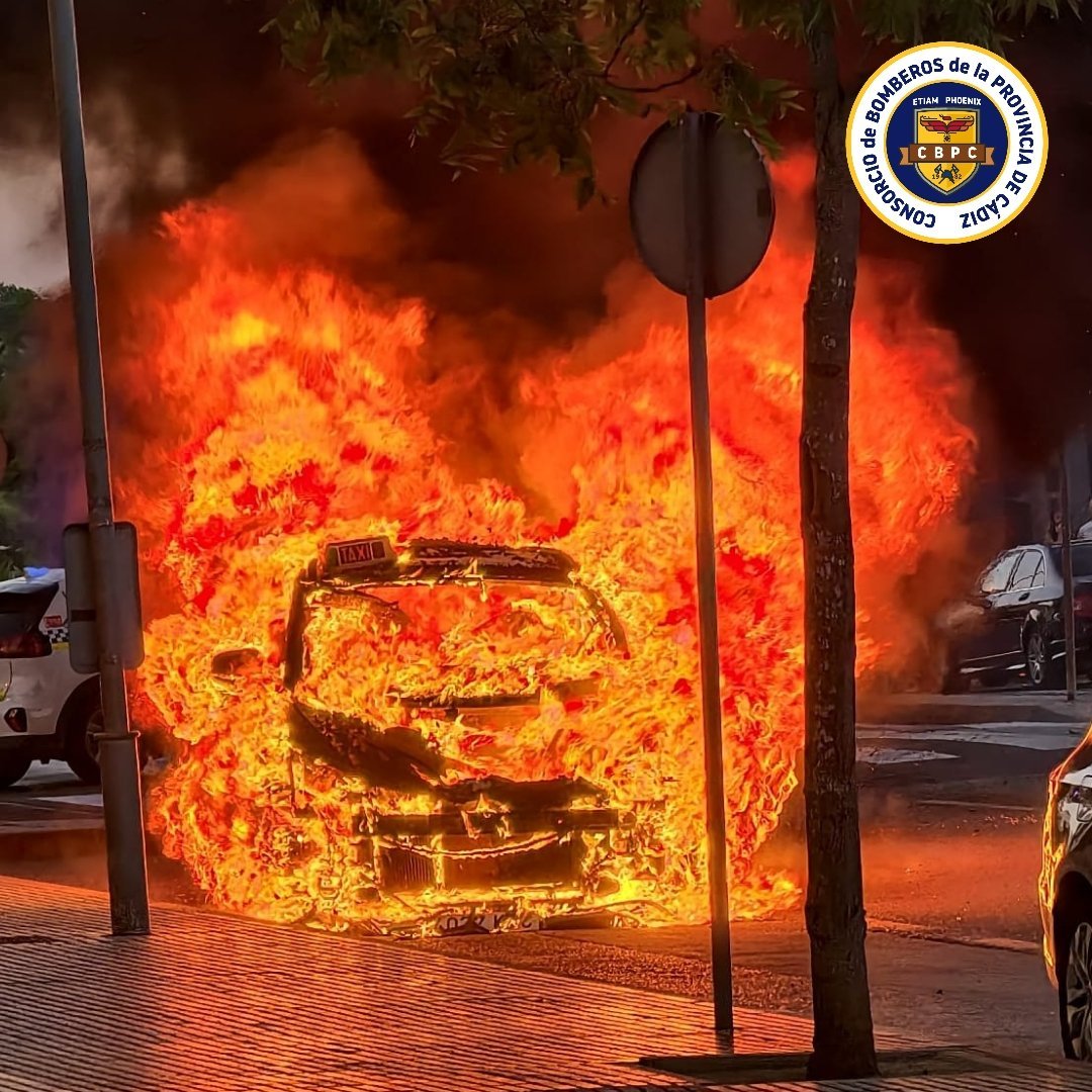 Taxi microhíbrido envuelto en llamas en la avenida Juan Carlos I de Jerez de la Frontera durante la intervención del Consorcio de Bomberos.