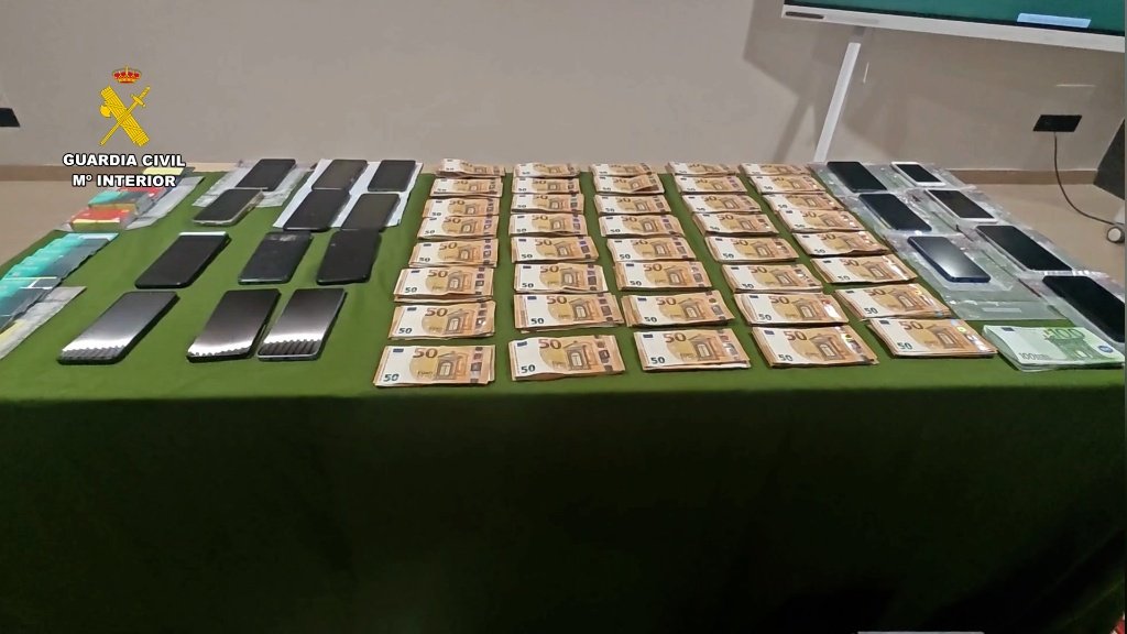 Mesa de la Guardia Civil mostrando fajos de billetes de 50 euros y numerosos teléfonos móviles incautados como parte de una estafa bancaria.