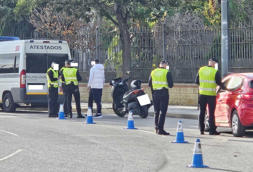 Varios agentes de la Policía Local de Jerez realizan un control de tráfico y alcoholemia a conductores de ciclomotores y coches en una calle de la ciudad. Se observa un furgón de atestados y conos azules delimitando la zona.