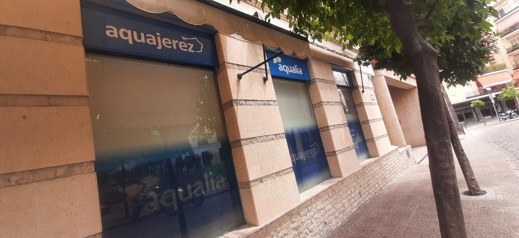 Fachada de la oficina de atención al público de Aquajerez en Jerez con cartelería de Aqualia sobre ventanales de cristal.