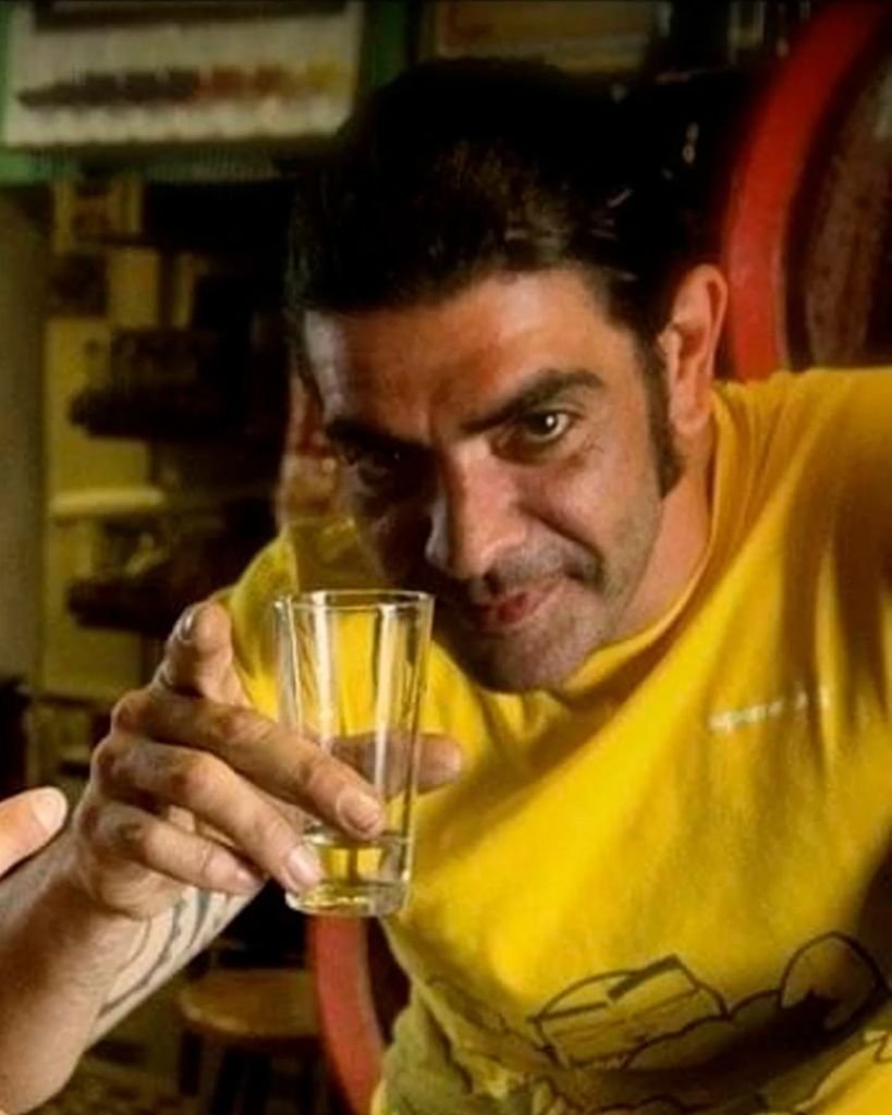 Retrato de David de la Chica "Davile" con camiseta amarilla señalando a cámara mientras sostiene un catavinos en un tabanco de Jerez.