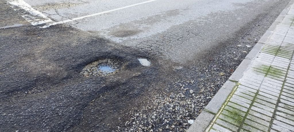 Detalle del asfalto degradado con piedras sueltas y agua en la avenida Nazaret de Jerez