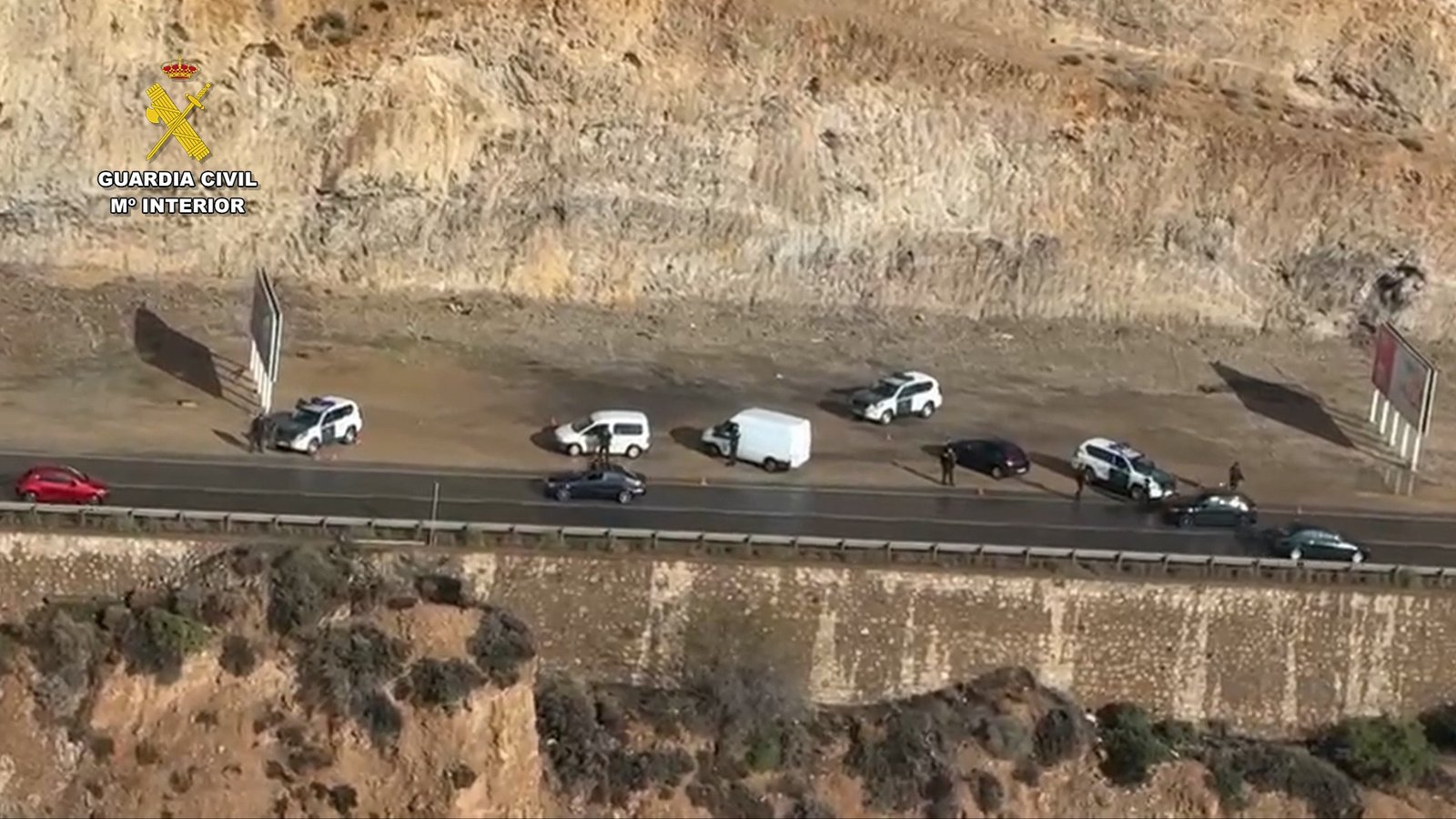 Dispositivo terrestre de la Guardia Civil en una carretera de la costa con múltiples vehículos patrulla y agentes interceptando turismos y furgonetas.