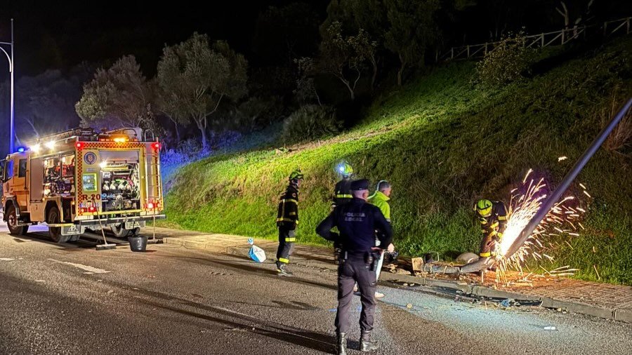 Bomberos y operarios municipales trabajando con herramientas de corte para retirar una farola dañada tras un accidente de tráfico en Medina Sidonia.