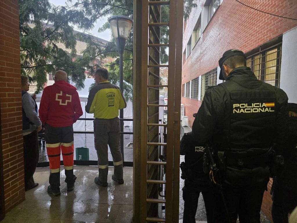 Agentes de la Policía Nacional de espaldas observando a miembros del GREA y Cruz Roja en un punto de atención durante la emergencia ferroviaria.