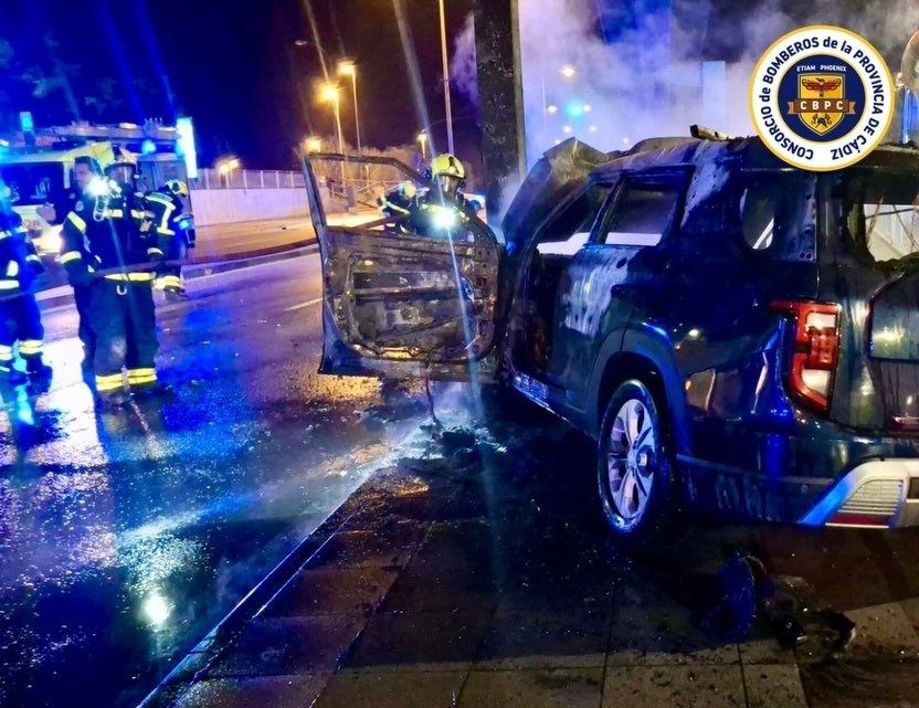 Bomberos de Jerez extinguiendo el fuego de un coche calcinado tras chocar contra un pilar en la Avenida Reina Sofía.