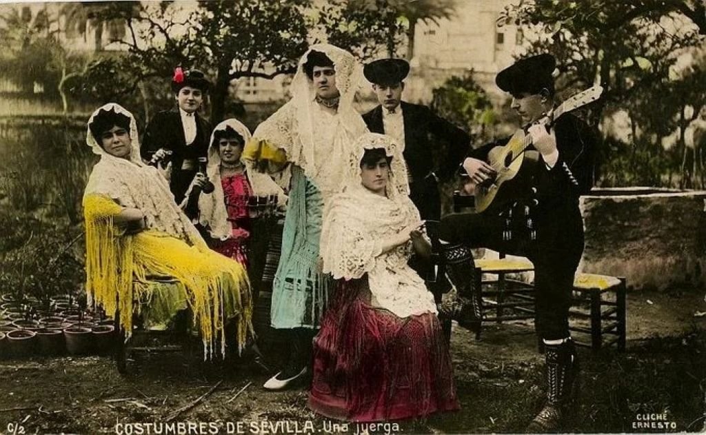 Postal antigua coloreada titulada Costumbres de Sevilla una juerga flamenca antigua con guitarrista y mujeres vestidas con mantones de Manila del archivo del CADF.