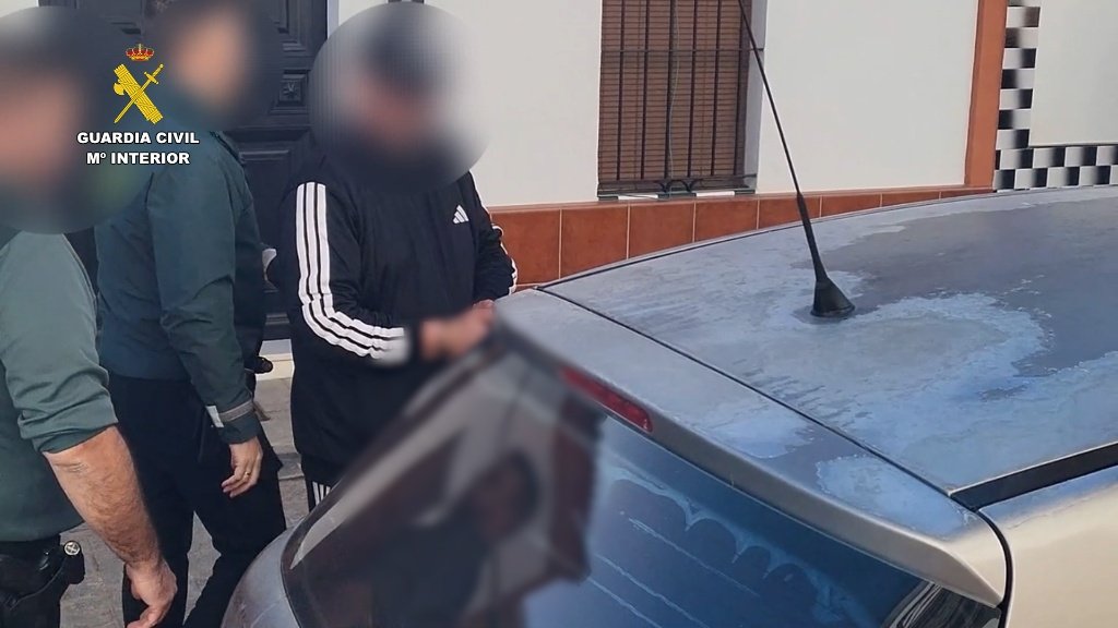 Agentes de la Guardia Civil escoltan a un hombre detenido junto a un vehículo por instalar una cámara oculta en un dormitorio.