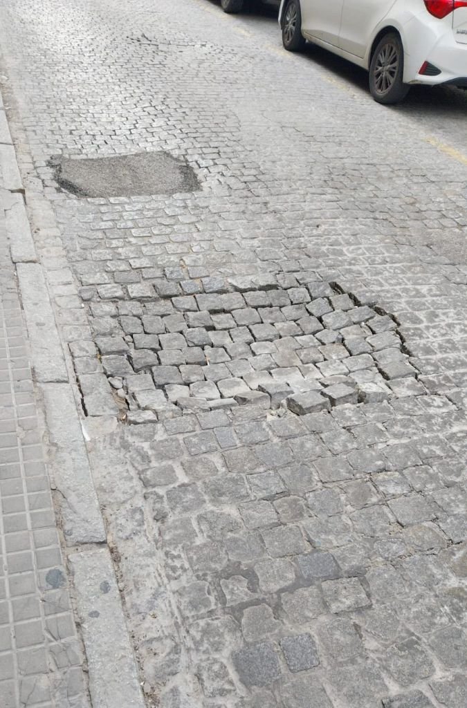 Socavón profundo en el adoquinado de la calle Caballeros en Jerez junto a un coche blanco estacionado.