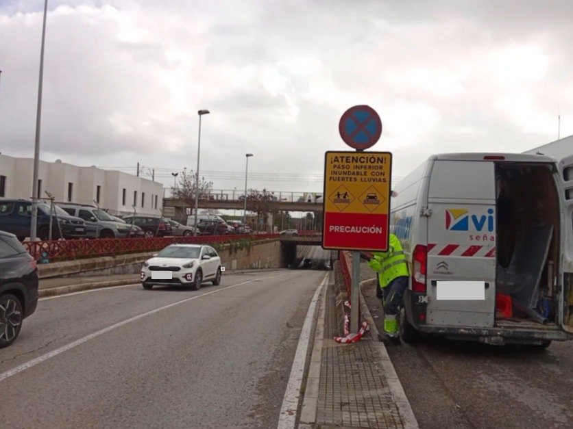 Operario instalando señal de tráfico de advertencia por paso inferior inundable en Jerez junto a una carretera con tráfico moderado.