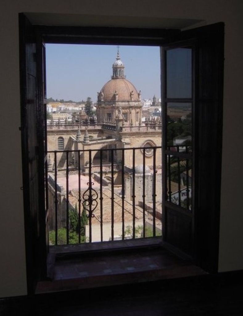 Vista de la cúpula de la Catedral de Jerez de la Frontera enmarcada por una ventana de madera abierta desde el Alcázar.