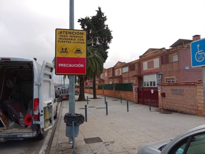 Señal de atención por paso inferior inundable ubicada en una acera de una zona residencial de Jerez con viviendas unifamiliares al fondo.