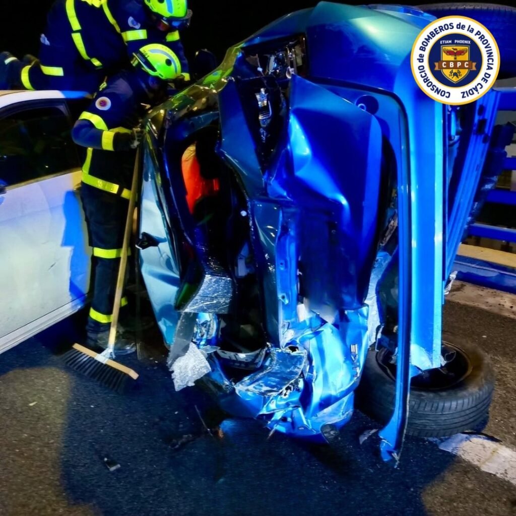 Primer plano de coche azul volcado tras colisión en la CA-35, con un bombero estabilizando la estructura para el rescate.