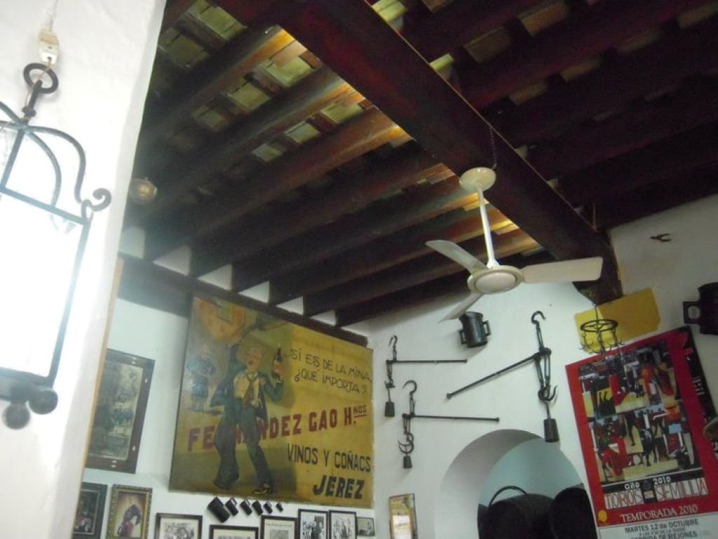 Cartel publicitario antiguo de vinos y coñacs de Jerez junto a una escala de pesaje y carteles taurinos.