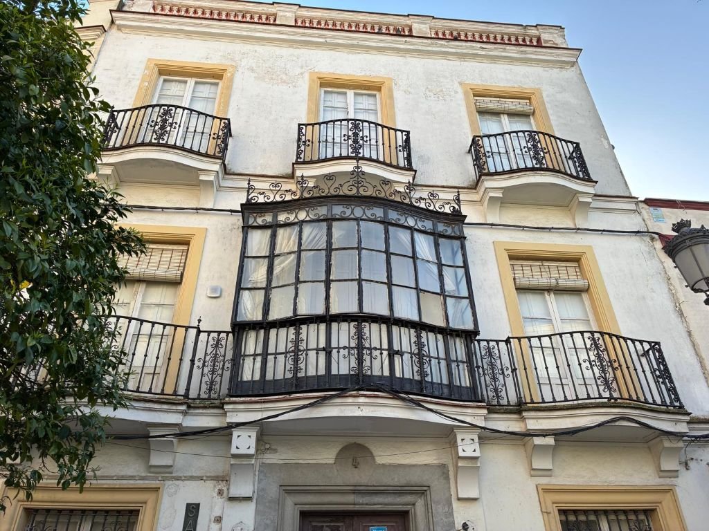 Calle del centro de Jerez que muestra el contraste entre un edificio conservado y una gran finca abandonada con muros de piedra deteriorados al fondo.