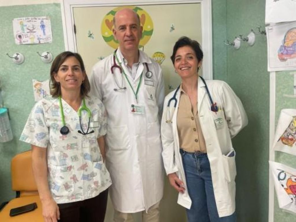 Fotografía de archivo del Servicio Andaluz de Salud (SAS) que muestra a tres profesionales médicos del Servicio de Pediatría del Hospital Universitario de Jerez. Los tres facultativos posan de pie en un pasillo hospitalario con decoración infantil de dibujos en las paredes. El profesional del centro es el Dr. David Gómez-Pastrana, jefe de Pediatría, flanqueado por dos pediatras del equipo, todos con batas blancas y estetoscopios al cuello.