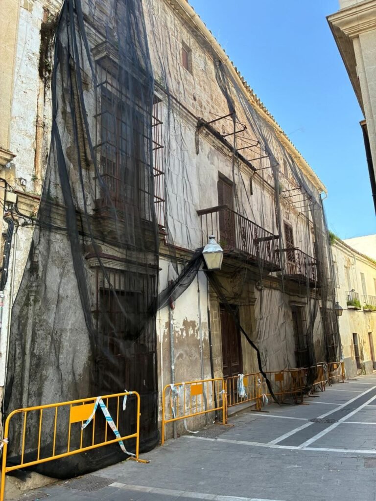 Edificio histórico en el centro de Jerez cubierto íntegramente con mallas de protección negras y vallas de seguridad amarillas en la acera.