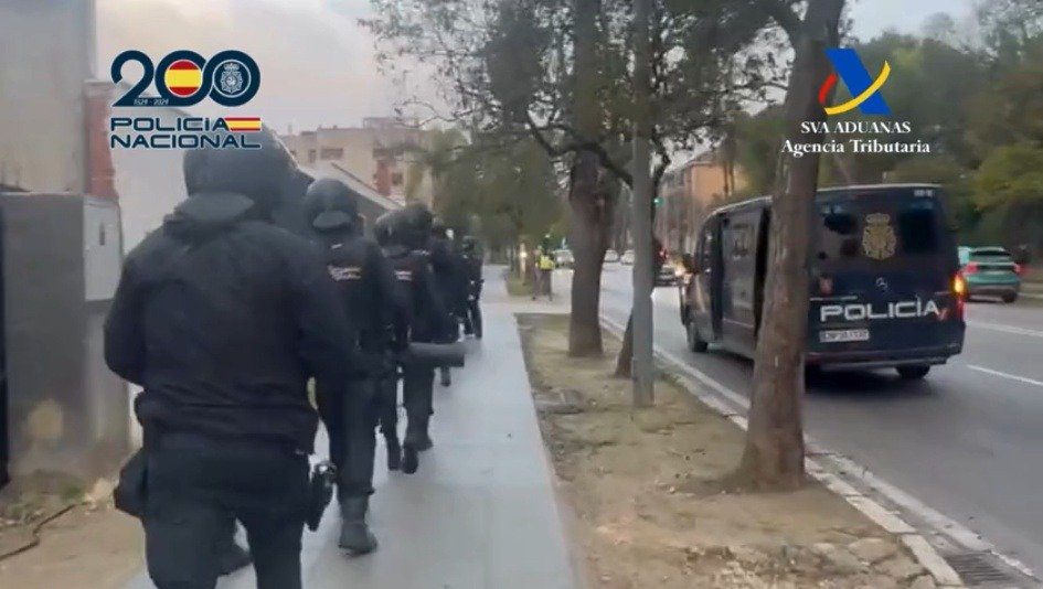 Fotografía de reportaje que recrea la masiva operación policial conjunta de la Policía Nacional y Vigilancia Aduanera bloqueando la Avenida de la Cruz Roja en Jerez. Muestra furgones, patrullas y agentes en uniforme táctico de ambas agencias realizando un registro a gran escala con la señalización urbana del Centro de Congresos y el Hotel Guadalete visible.