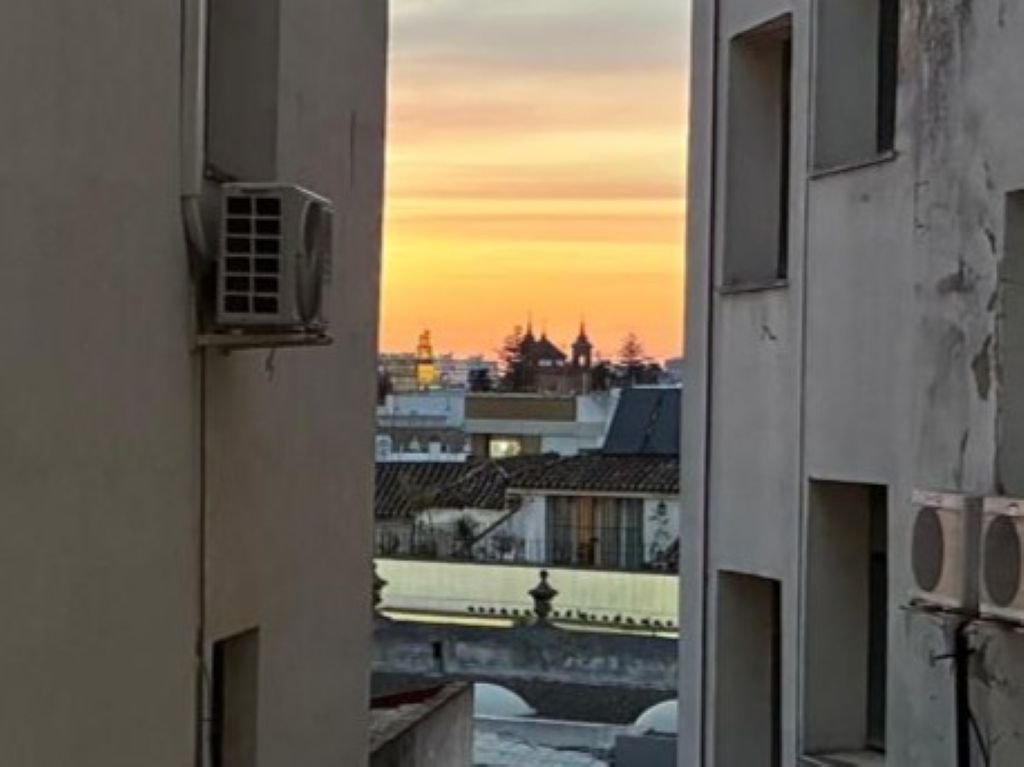 Silueta de la torre y cúpulas de iglesias en Jerez de la Frontera durante un atardecer naranja, enmarcada entre dos edificios residenciales del centro.