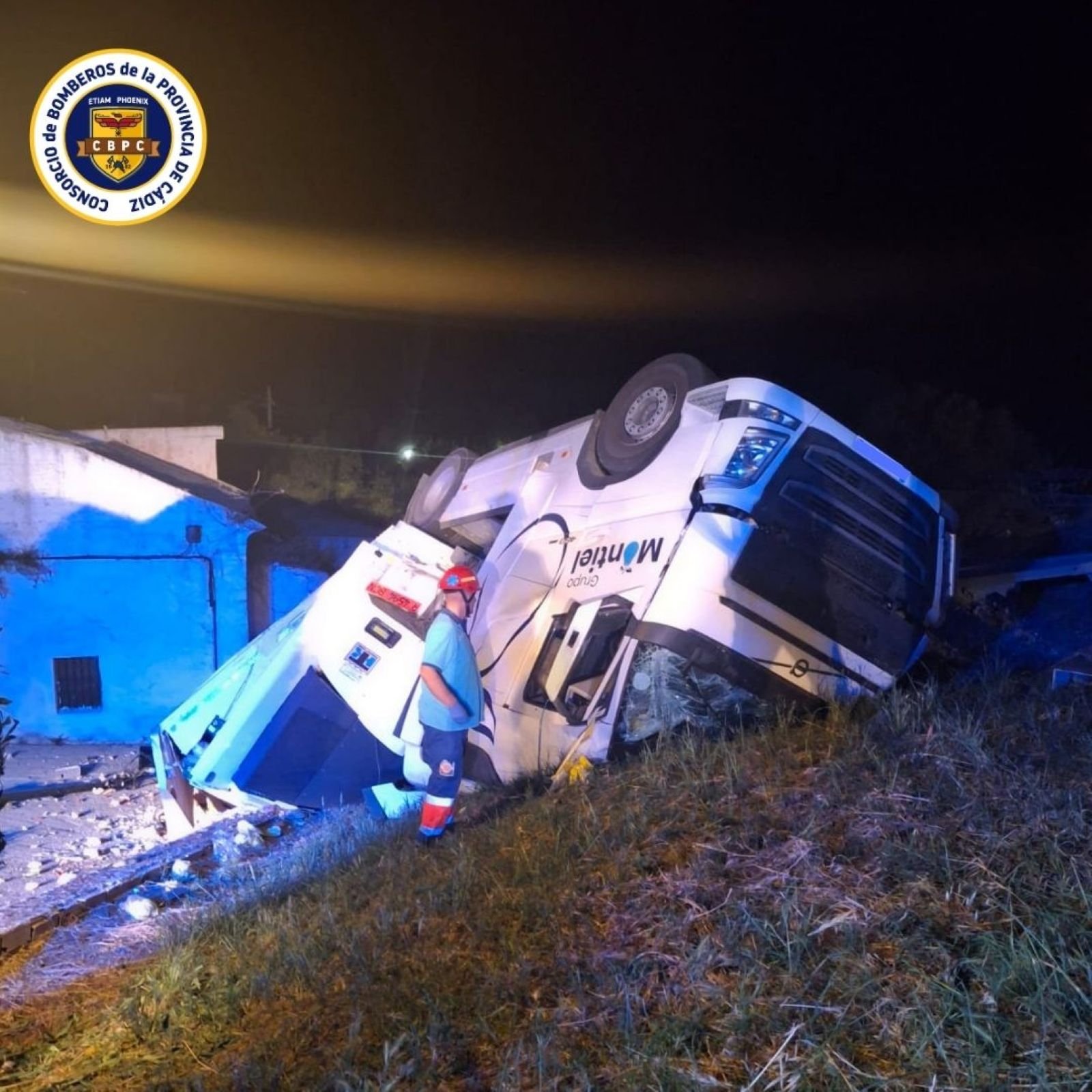 Camión articulado blanco volcado en la cuneta durante un accidente de tráfico nocturno en la carretera A348 en Villamartín con un bombero supervisando la zona.