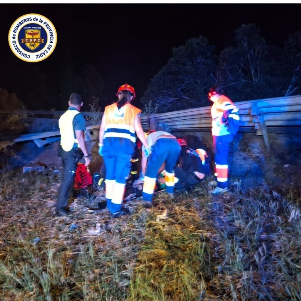 Sanitarios de emergencias y bomberos atendiendo al conductor herido sobre la hierba tras ser rescatado de la cabina del camión en Villamartín.