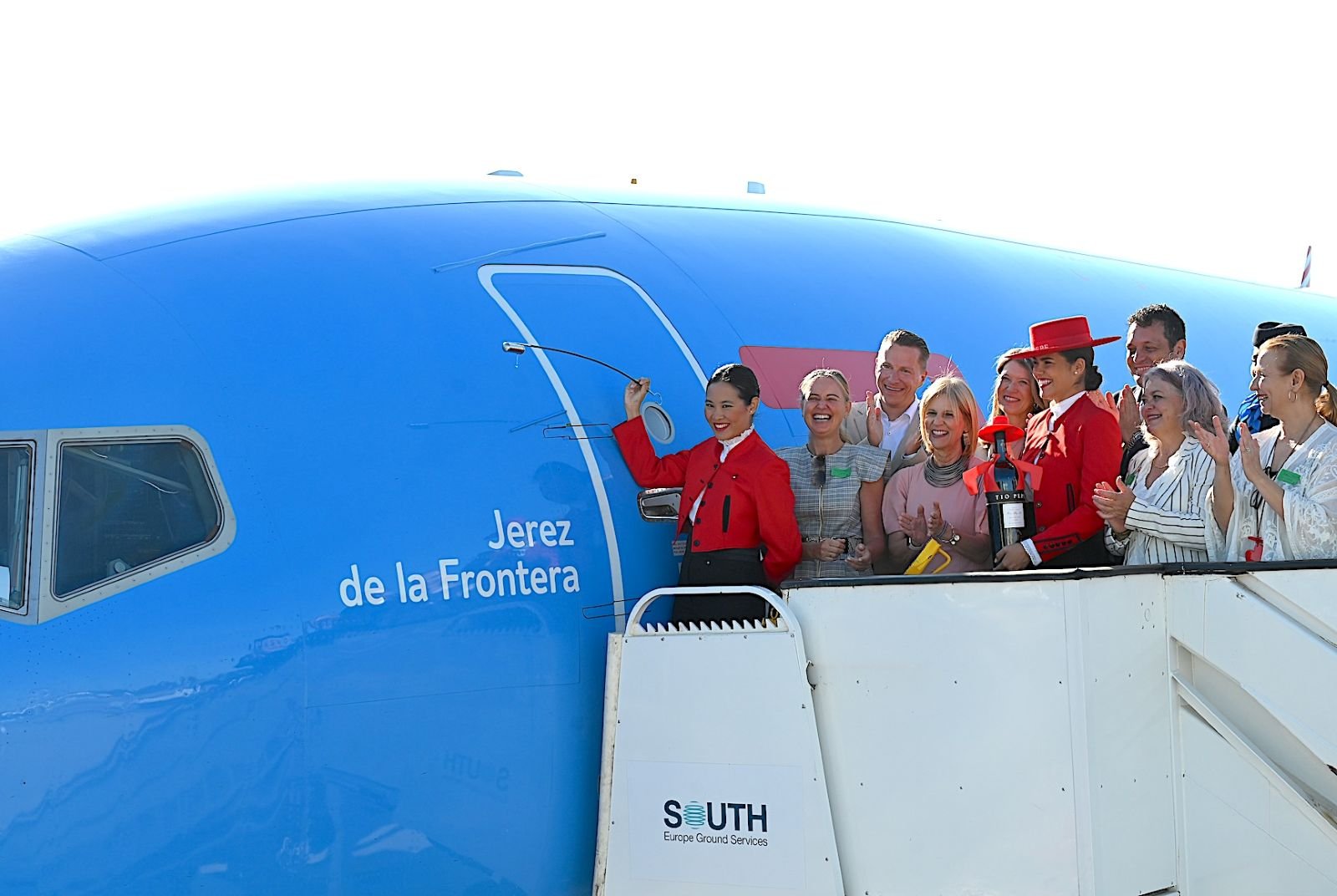 Comitiva sonriente en la escalerilla del avión Boeing 737 de TUI, junto a la inscripción "Jerez de la Frontera" en el fuselaje azul durante el bautizo de la aeronave.