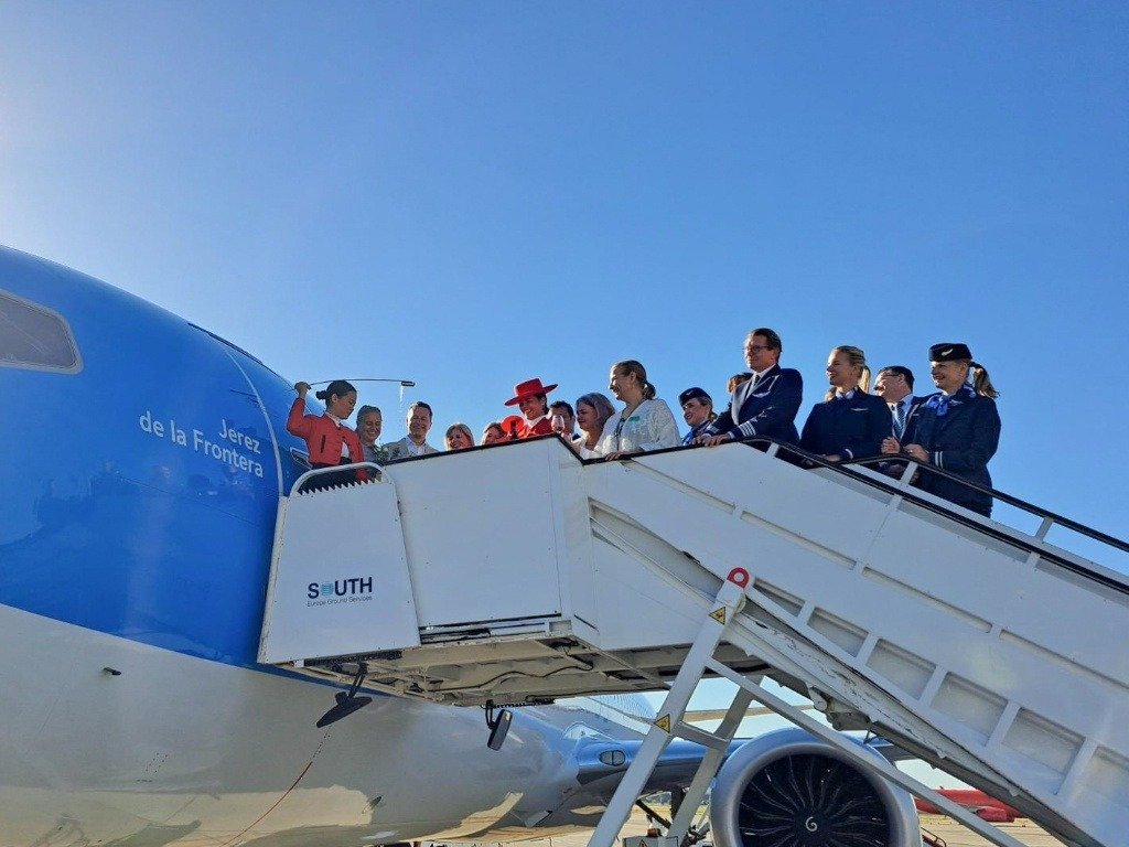 Comitiva oficial e invitados sobre la escalinata del avión de TUI en el Aeropuerto de Jerez mientras una venenciadora de González Byass realiza el tradicional bautizo con vino de la tierra.