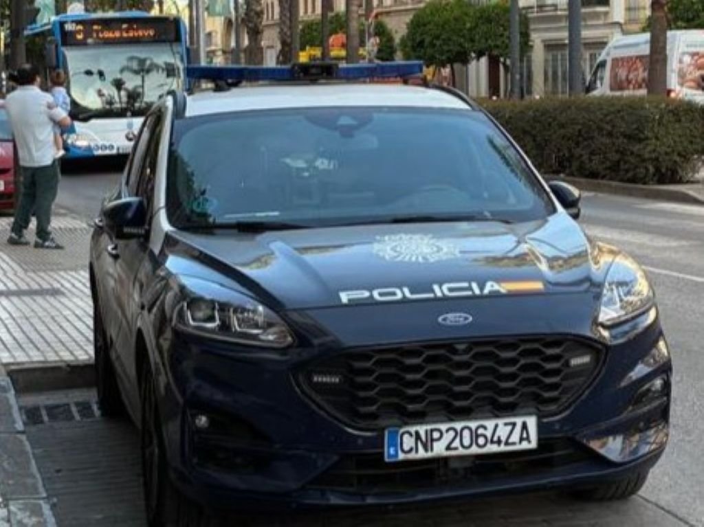 Coche patrulla de la Policía Nacional estacionado en una avenida urbana de Jerez de la Frontera, con un autobús de línea al fondo.