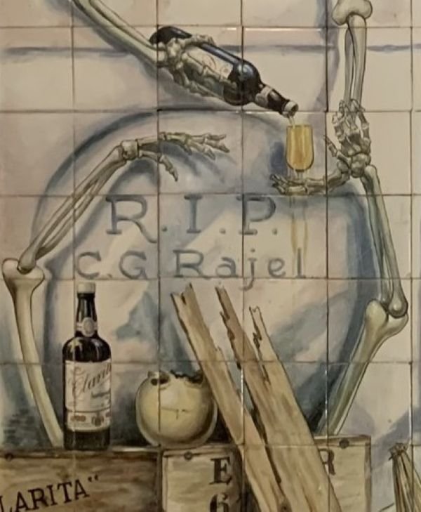 Detalle del epitafio y firma humorística de Carlos González Ragel pintada con jota en la cerámica.