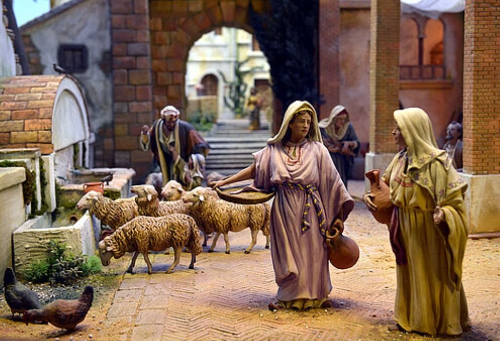Diorama detallado de un pueblo antiguo con figuras de pastoras portando vasijas junto a un rebaño de ovejas.