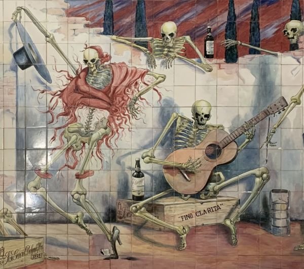 Esqueletos flamencos bailando y tocando la guitarra en un retablo cerámico de Jerez.