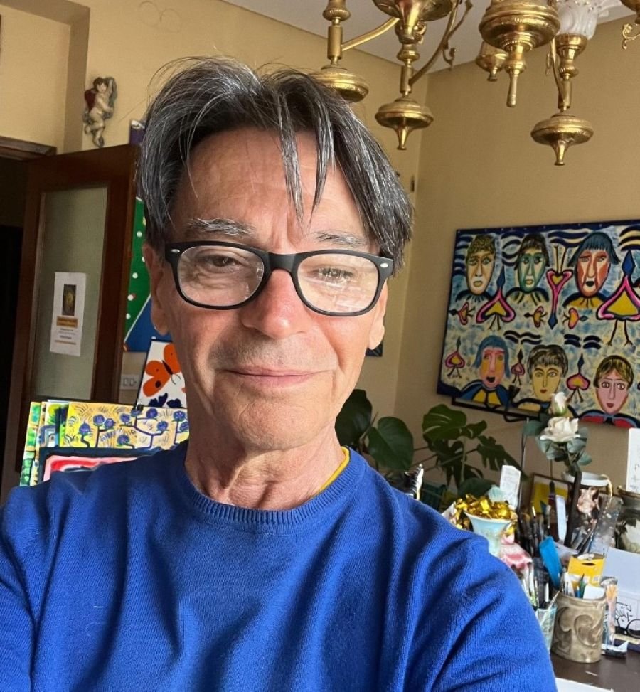 Primer plano del pintor Jean Paul Pallard con una de sus pinturas surrealistas de rostros al fondo.