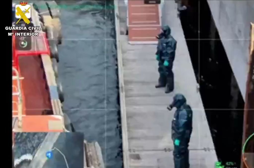 Dos operarios con trajes de protección NBQ azules y máscaras de gas en la pasarela de desembarco.