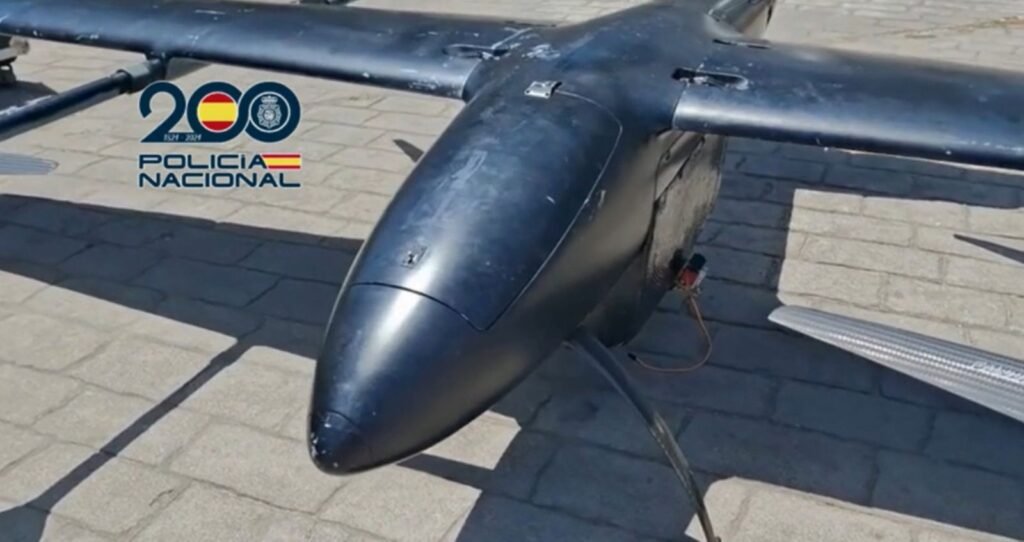 Primer plano frontal del morro y las alas de un dron gigante de color negro mate empleado por narcotraficantes, fotografiado en el exterior sobre suelo pavimentado con el logotipo oficial de la Policía Nacional.