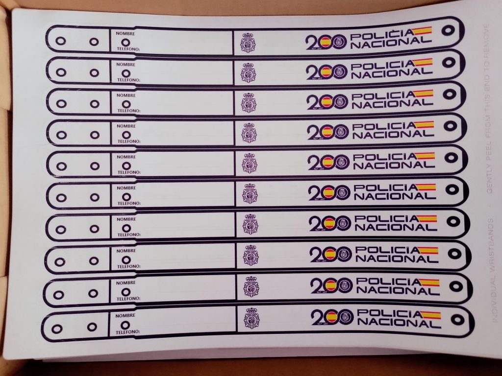 Primer plano de una hoja con múltiples pulseras identificativas de vinilo de la Policía Nacional, listas para ser usadas. Tienen espacios en blanco para escribir el nombre y el teléfono de contacto de los padres.
