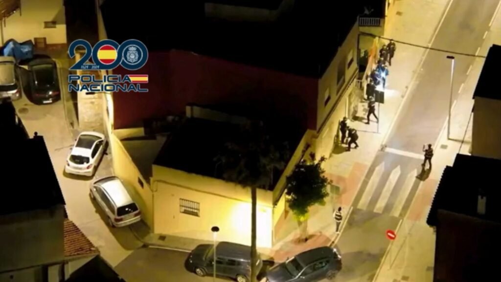 Vista aérea nocturna de agentes de la Policía Nacional realizando un registro domiciliario en una calle iluminada durante la Operación HORUS contra el narcotráfico.