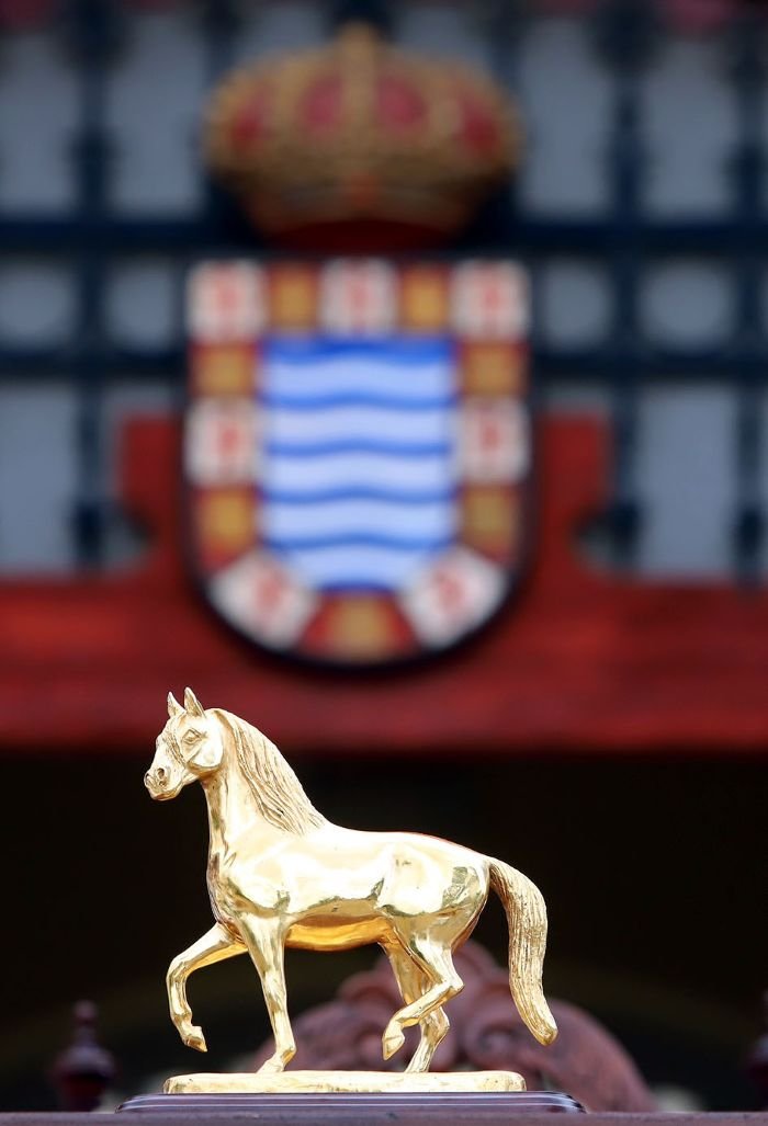 Estatuilla dorada del Caballo de Oro sobre un pedestal con el escudo de Jerez de la Frontera desenfocado al fondo.
