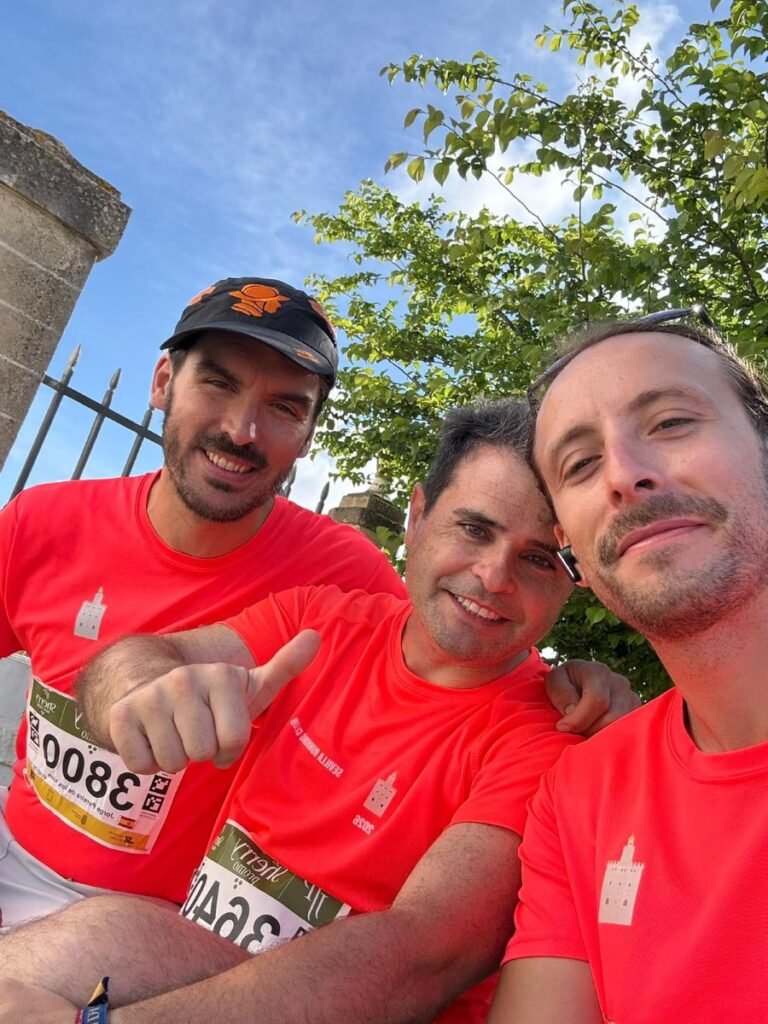 Tres corredores del Sevilla Running Club con camisetas naranjas sonríen tras completar la prueba en Jerez.