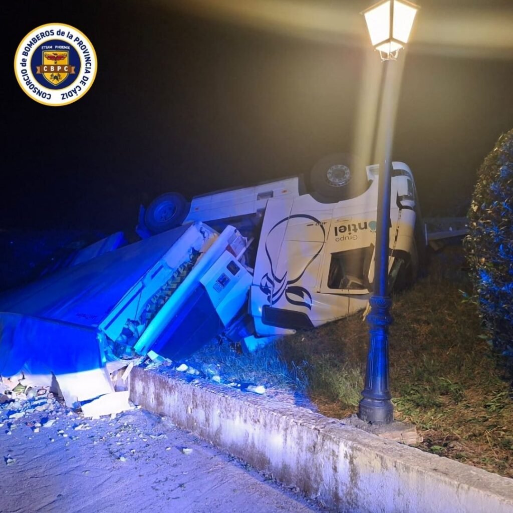 Perspectiva nocturna del camión volcado tras una salida de vía en la A348 junto a una farola encendida y restos de la carga sobre el arcén.
